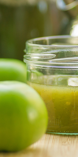 Einmachglas mit grüner Tomaten-Konfitüre und einigen grünen Tomaten