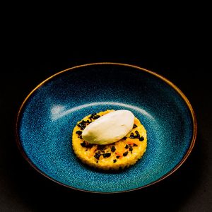 Orangen-Milchreis mit weißem Kaffee-Eis und kandieten schwarzen Oliven auf einem blauen Teller