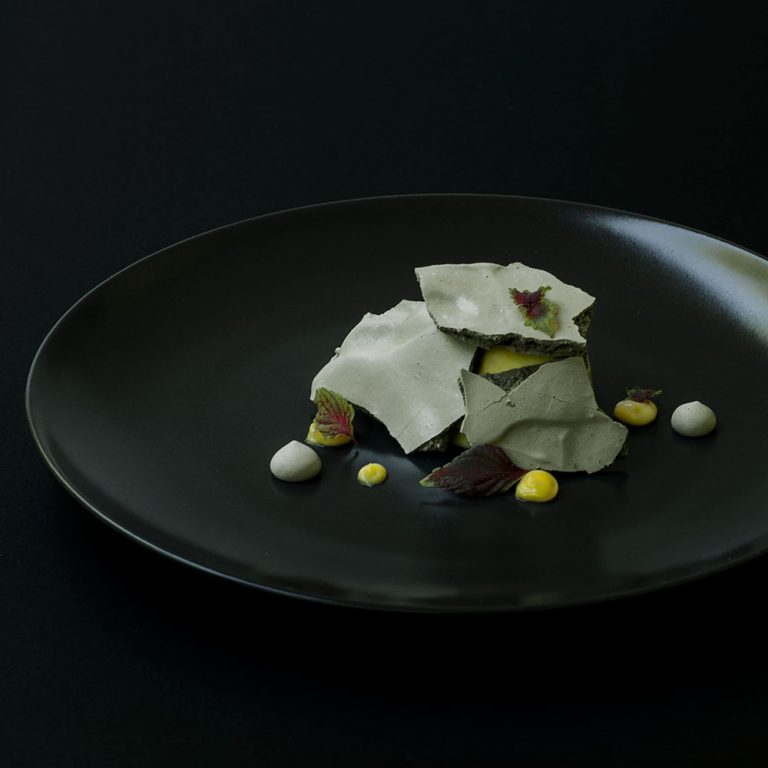 Teller mit Bergamotteneis bedeckt von Lakritzbaiser-Platten mit bergamot Curd und roten Shiso-Blättern.