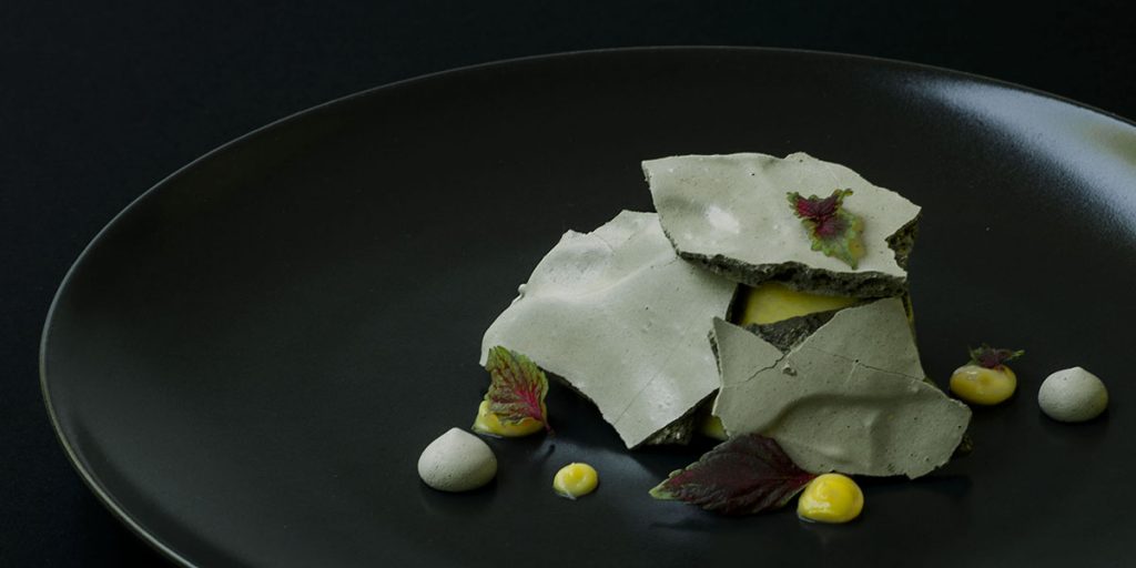 Teller mit Bergamotteneis bedeckt von Lakritzbaiser-Platten mit bergamot Curd und roten Shiso-Blättern.