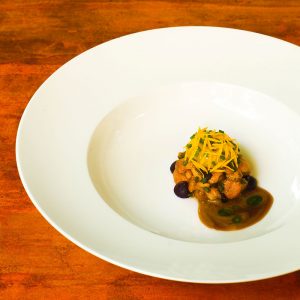 Teller mit cremigen Pfifferlingen, confiertem Eigelb, Heidelbeer-Zwiebel-Creme, Pilzfond und Kiefernöl.